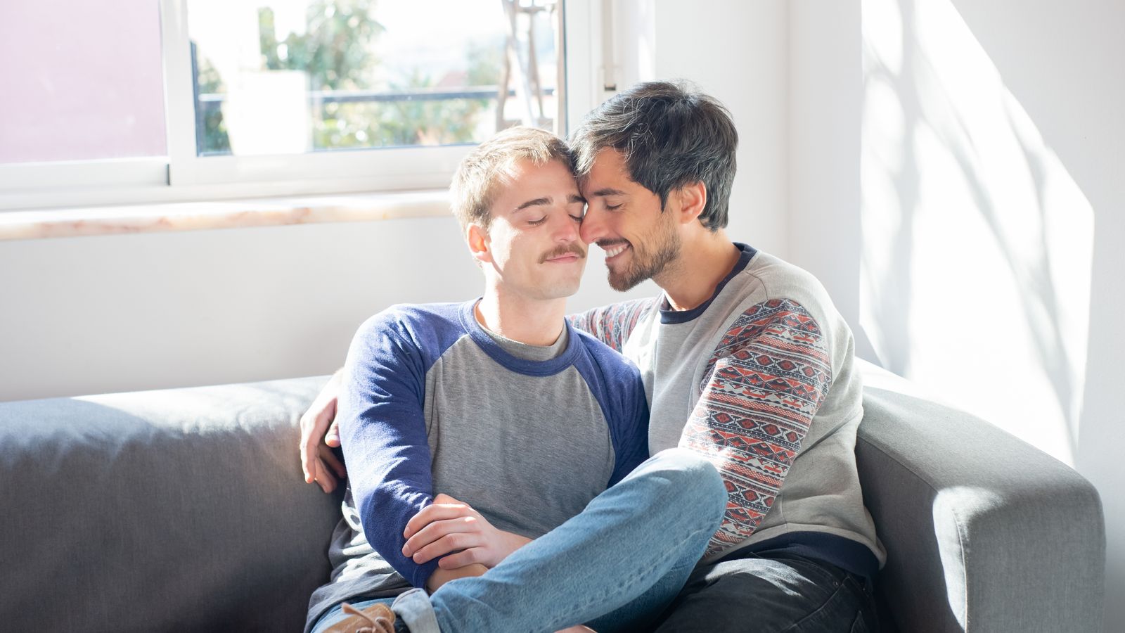 Two adults cuddling while seated on a sofa in a sunlit room