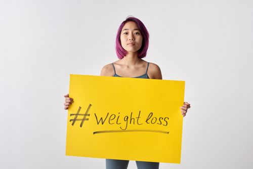 Free Asian woman with purple hair holding a weight loss sign in a studio setting. Stock Photo