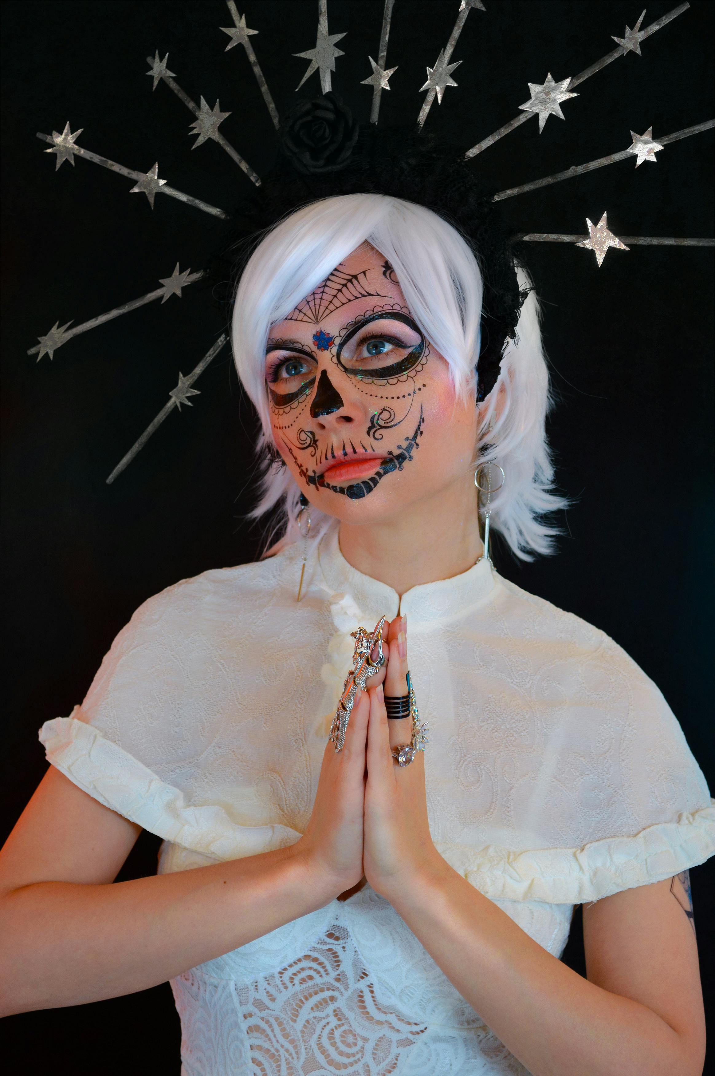 concentrated young woman with halloween makeup and costume praying in black studio