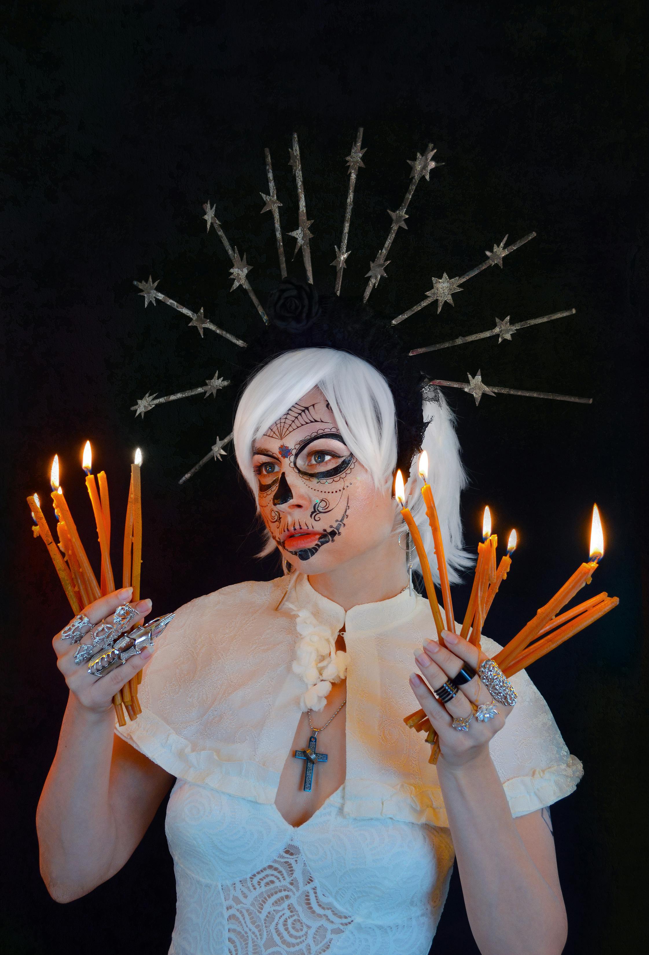 young woman in calavera catrina costume standing in black studio with burning candles