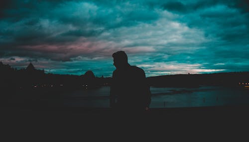 Free Man Silhouette Near Body of Water at Nighttime Stock Photo