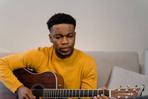 Free A man in a yellow sweater plays an acoustic guitar while sitting in a cozy indoor setting. Stock Photo