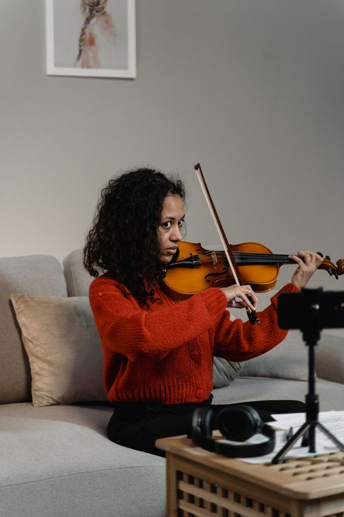 Free African American woman playing violin on a couch indoors, captured in a vertical frame. Stock Photo