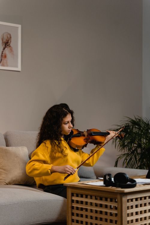 Free Young girl plays violin indoors, showcasing talent in a cozy living room. Stock Photo