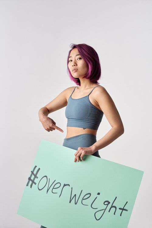 Free Confident woman with purple hair in activewear holding #overweight sign promoting body positivity. Stock Photo