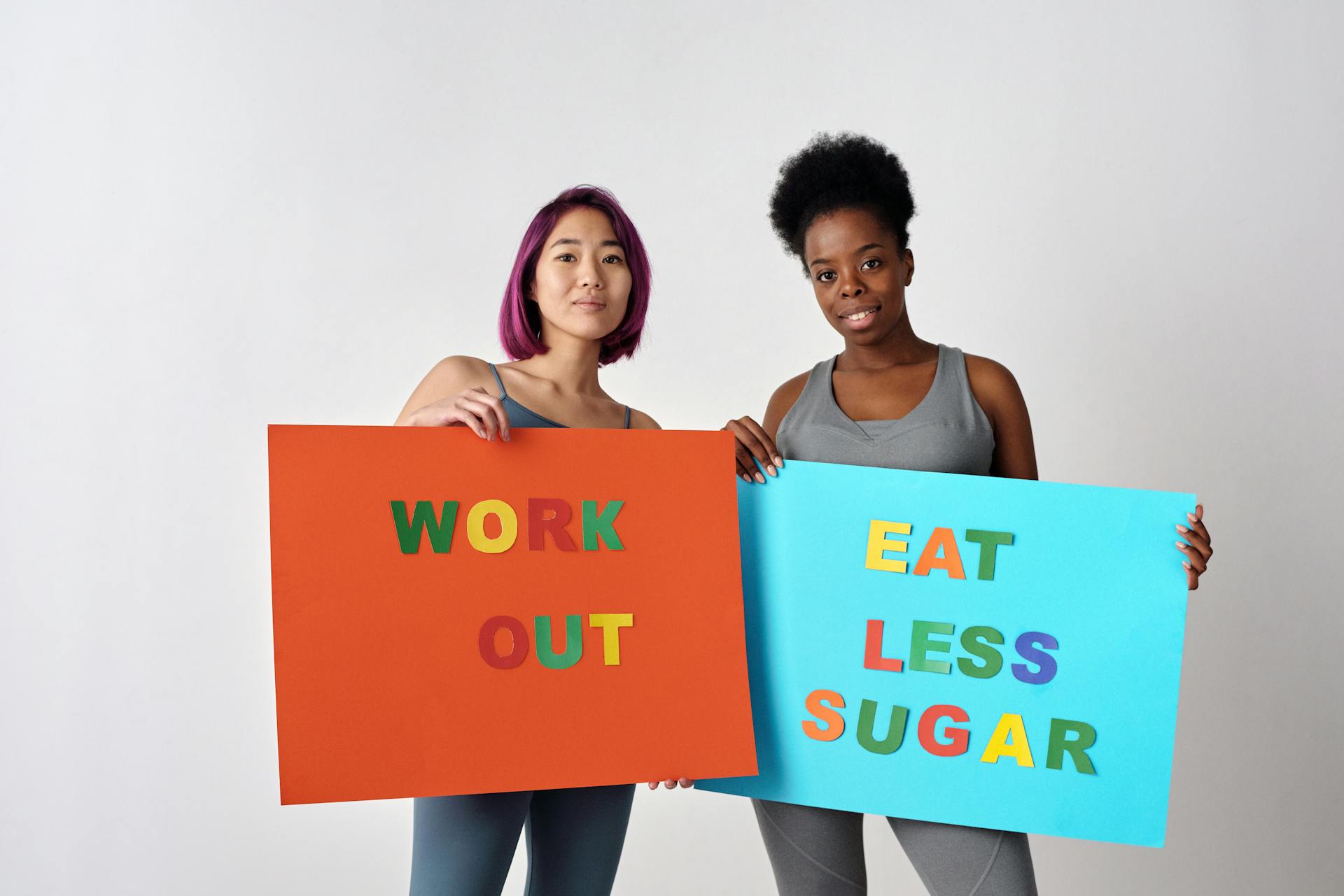 Two women holding motivational posters promoting healthy lifestyle changes against a white background.