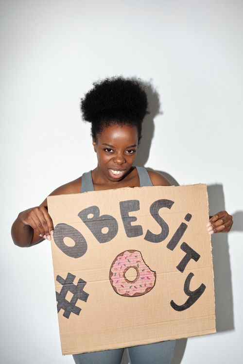 Free A woman holds a cardboard sign promoting obesity awareness with a colorful design. Stock Photo