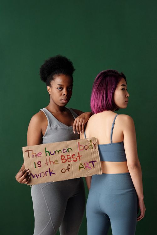 Free Two women in activewear holding a sign with an inspirational quote about body positivity in a studio setting. Stock Photo