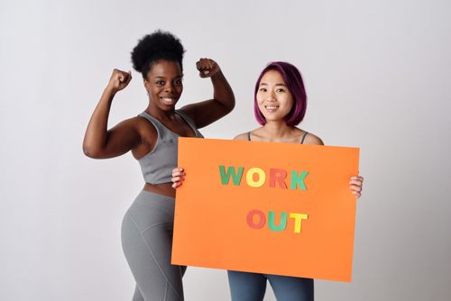 Free Two women in activewear holding a workout sign, encouraging fitness. Stock Photo