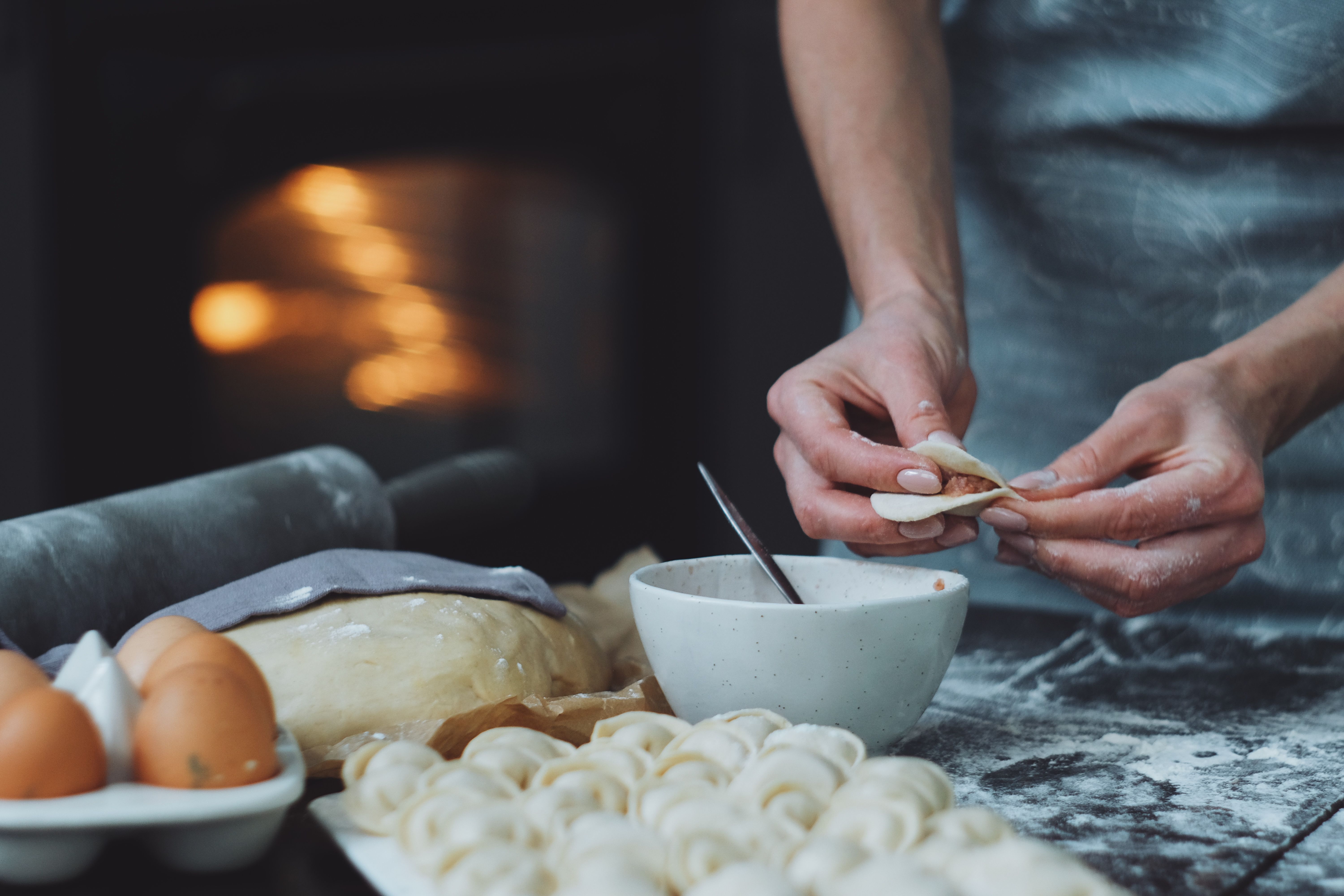Close-up of hands crafting dumplings with fresh ingredients, dough and eggs nearby.