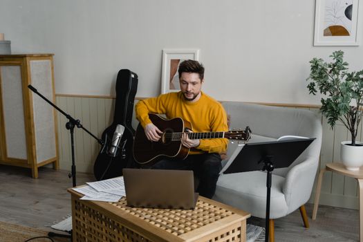 Man in yellow sweater playing guitar in a cozy living room setup for a virtual music performance.