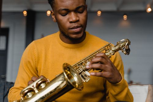 Free Young black male saxophonist playing indoors, wearing a yellow sweater. Stock Photo