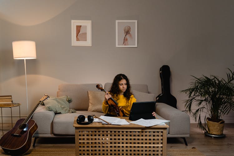 Teenage Girl In Mustard Long Sleeve Shirt Holding A Violin And Using A Tablet 