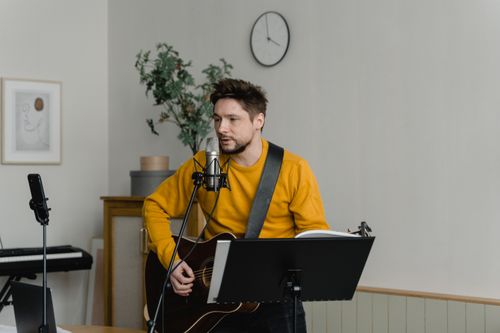 Free A man in a yellow sweater sings and plays guitar indoors, using a microphone. Stock Photo
