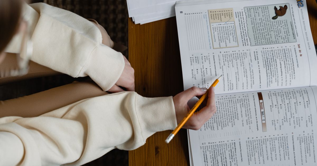 A student studying from an open book, holding a pencil, indoors.