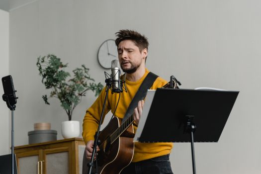Musician playing guitar and singing indoors with microphone and music stand.