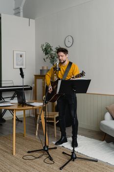Adult musician playing guitar and singing in a cozy home studio.