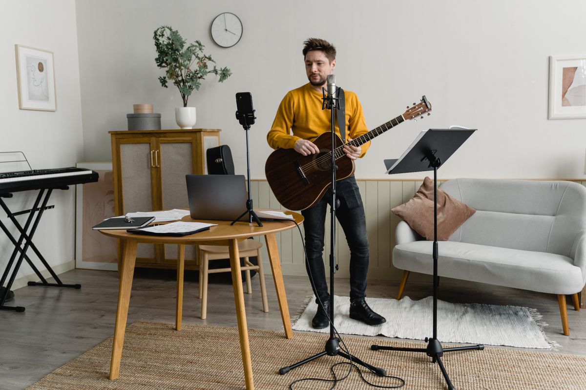 Man playing acoustic guitar during music practice session indoors, with music equipment. Illustrative editorial photograph.