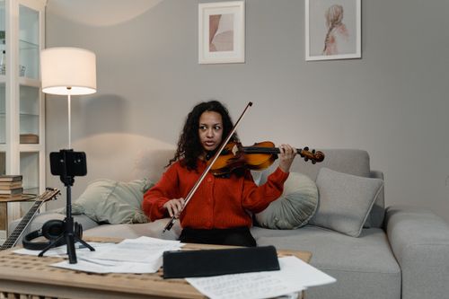 Free Woman playing violin on couch, creating a musical ambiance indoors. Stock Photo
