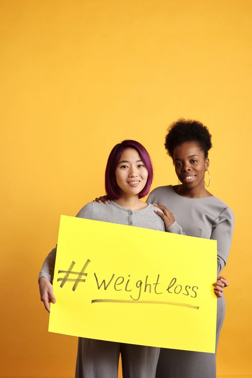 Free Two women promoting healthy lifestyle with weight loss message on a bold yellow background. Stock Photo