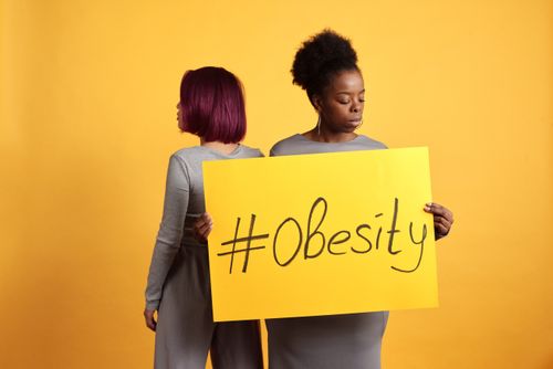 Free Two women advocate obesity awareness holding a bold sign with a vibrant yellow backdrop. Stock Photo