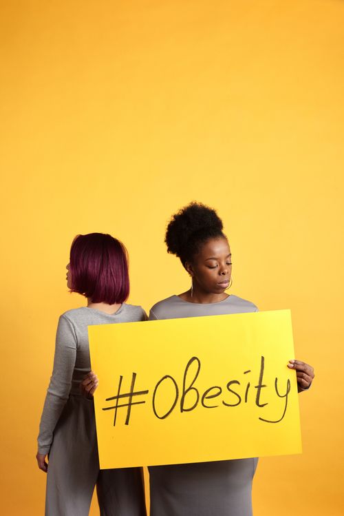 Free Two women holding a sign about obesity awareness with a vibrant yellow backdrop. Stock Photo