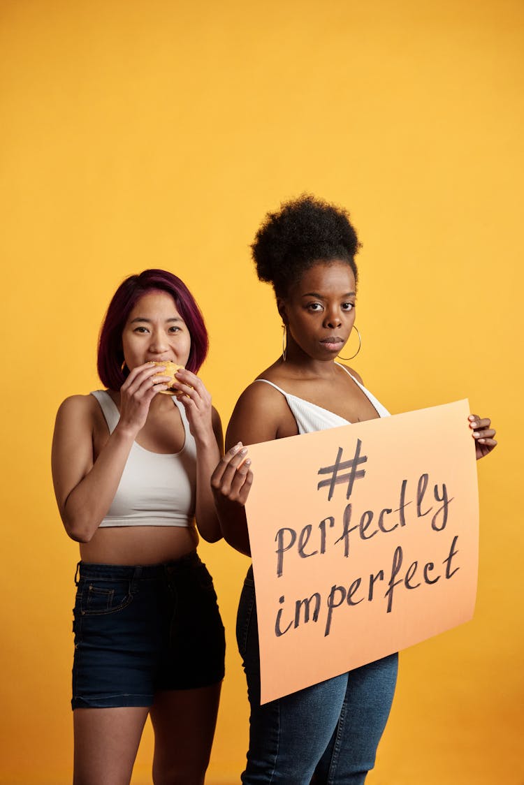 Women In White Crop Top Shirt Eating A Burger And Holding A Poster