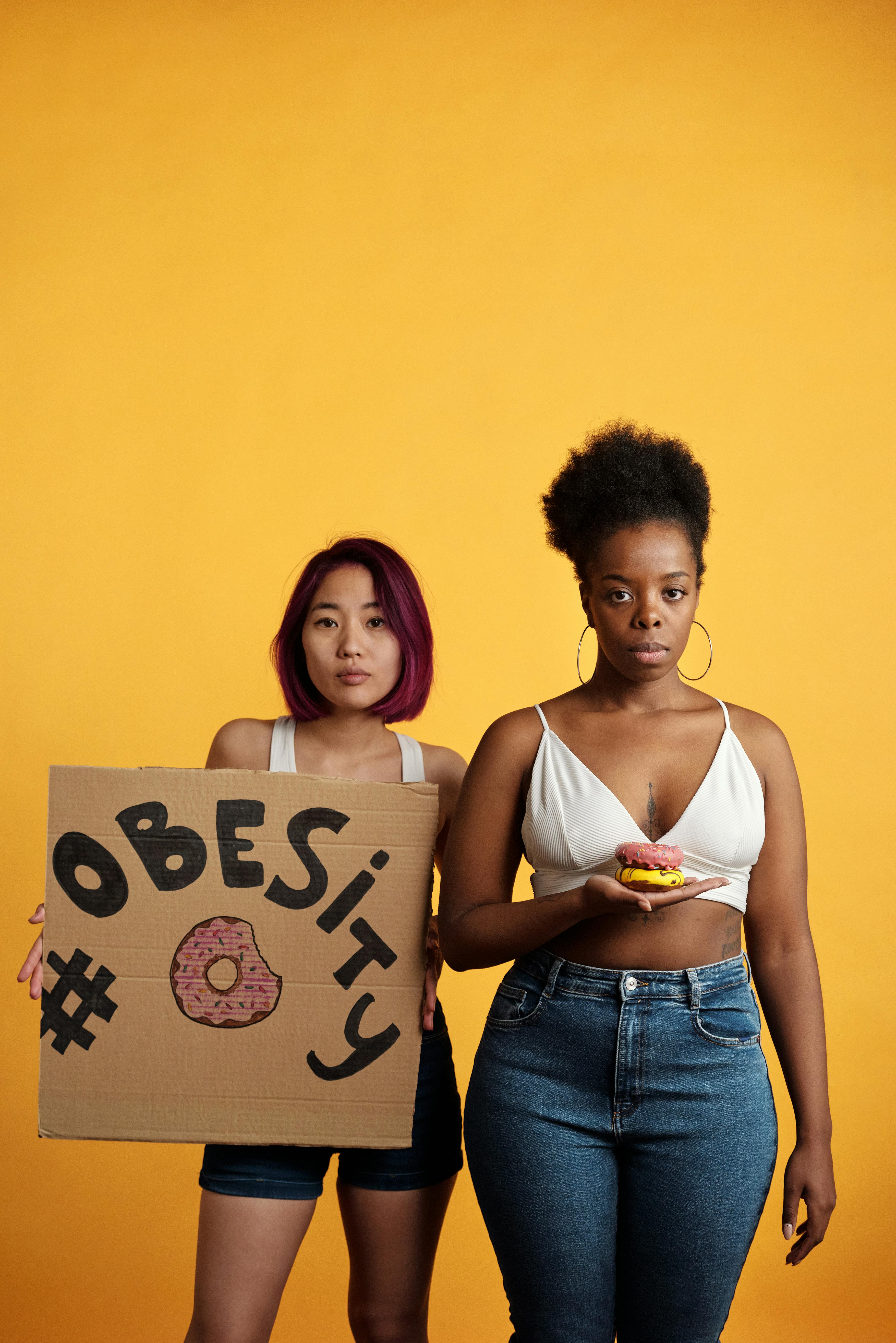 Two women highlighting obesity with a placard in a studio setting.