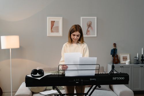 Free Teenage girl standing at a keyboard, reading sheet music in a cozy living room. Stock Photo