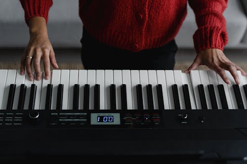 Person in Red Knitted Long Sleeves Playing Digital Piano