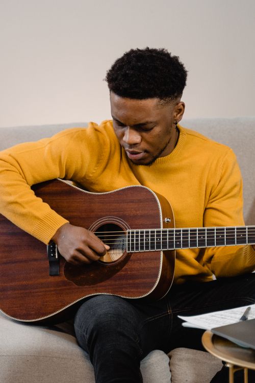 Free A young man sitting indoors, skillfully playing an acoustic guitar. Musical talent in action. Stock Photo
