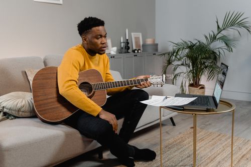 Free Man playing guitar while learning online in cozy home setting. Stock Photo