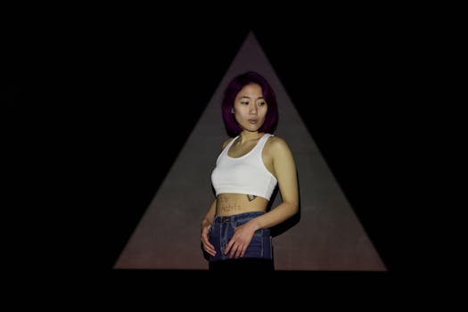 A stylish Asian woman in casual attire posing in a studio with a black triangular background.