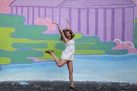 一名女子在充满活力的柔和壁画前高兴地跳起，捕捉到了有趣的户外瞬间