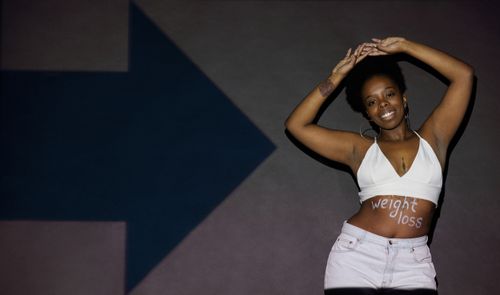 Free Smiling woman with afro hairstyle posing in a white bralette with 'weight loss' written on her torso. Stock Photo