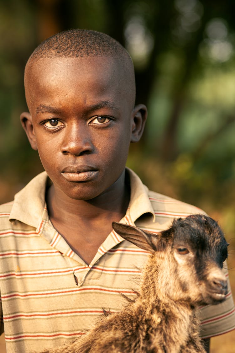 Concentrated Black Teen Boy Hugging Goat And Looking At Camera