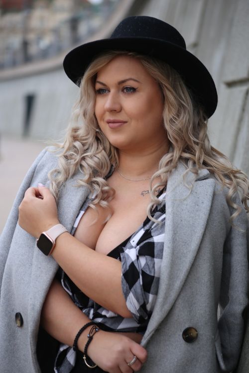 Free Fashionable woman with curly hair in a hat and coat, posing outdoors with a thoughtful expression. Stock Photo