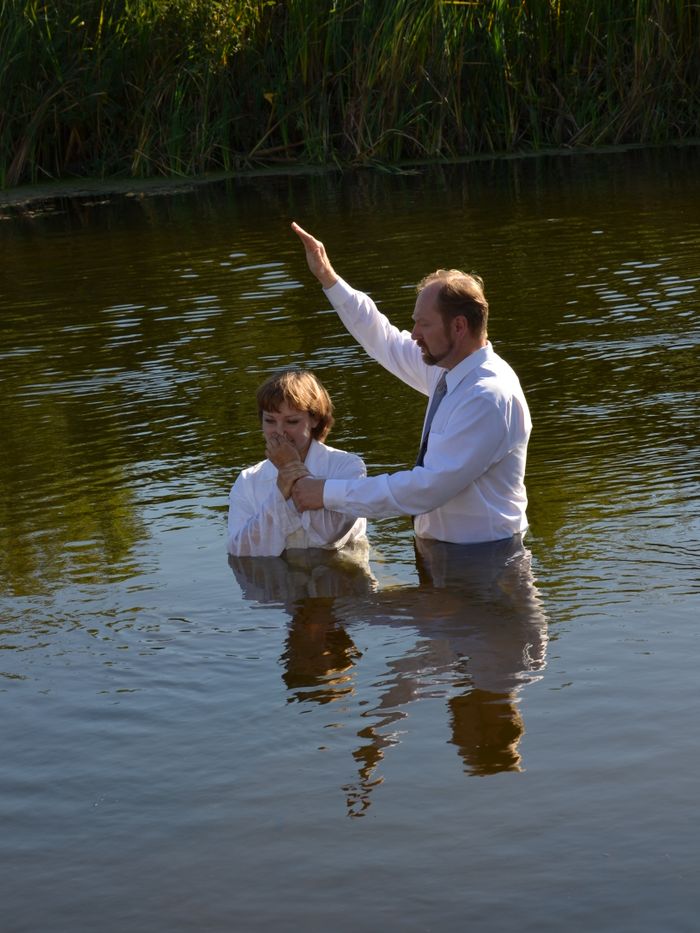Batismo por imersão em água, com o pastor abençoando o batizando