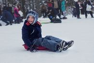A Young Kid in Winter Clothes Smiling while Sitting on a Sled