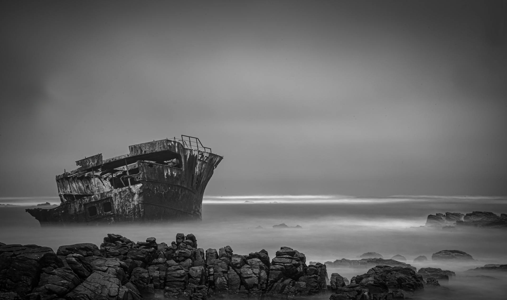 Eerie black and white photo of an abandoned shipwreck along South Africa's rocky coastline, evoking mystery and solitude.