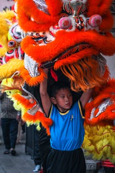 Young boy performing a traditional Chinese dragon dance during a vibrant festival parade. Captured in a lively outdoor setting.