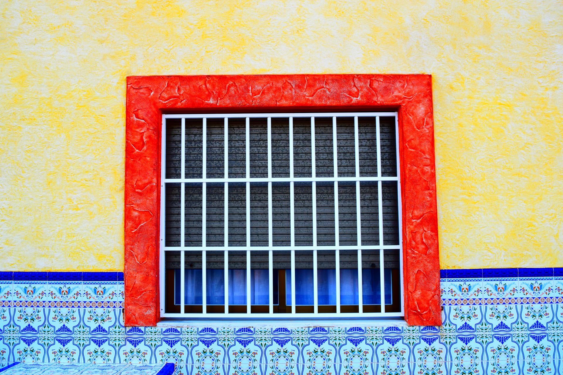 Colorful window with security bars surrounded by vibrant walls and intricate tiles.