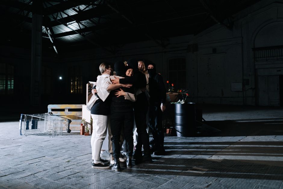 Un grupo diverso de adultos abrazándose en un espacio industrial con poca luz, simbolizando unidad.