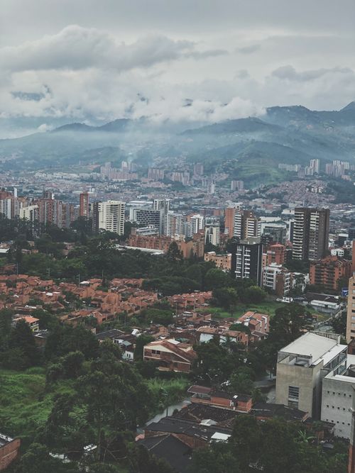 Free Aerial view of a cityscape with urban buildings and mountains in the background, under a cloudy sky. Stock Photo