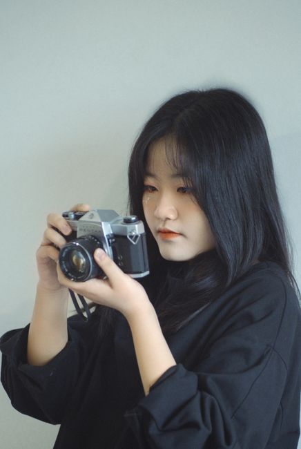 Asian woman holding a vintage camera, capturing candid moments. Perfect for photography themes.