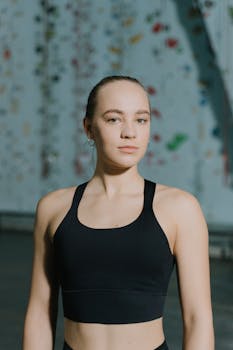 Focused young woman in activewear poses in a climbing gym setting.
