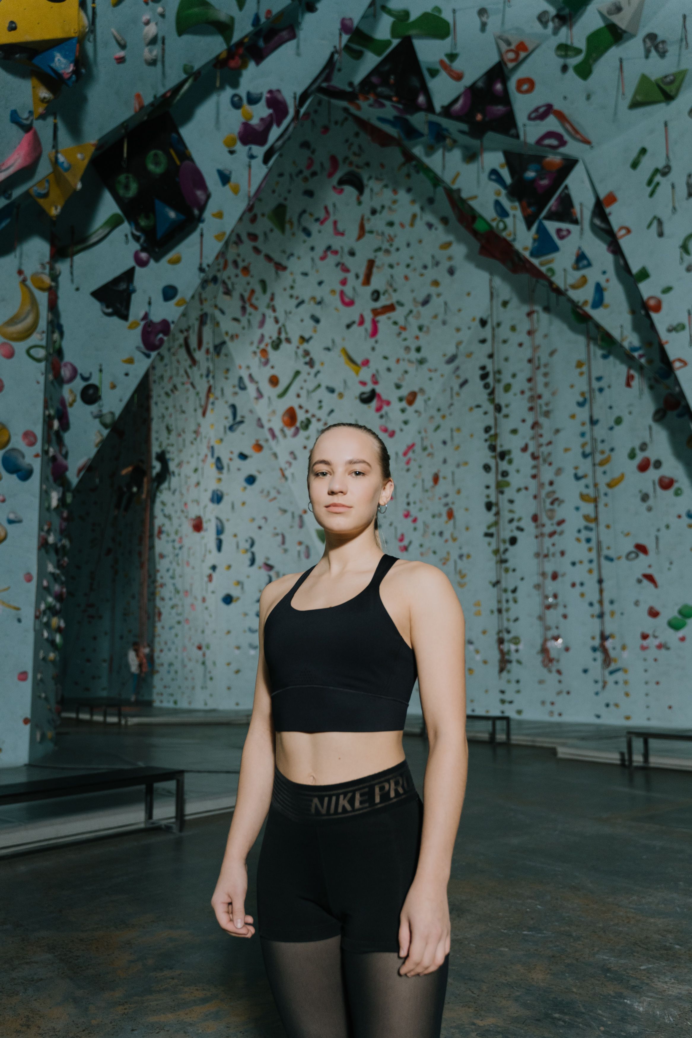 A young woman in activewear stands confidently at an indoor climbing gym.