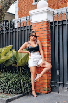 Stylish young woman in sunglasses posing by a brick wall in São Paulo.