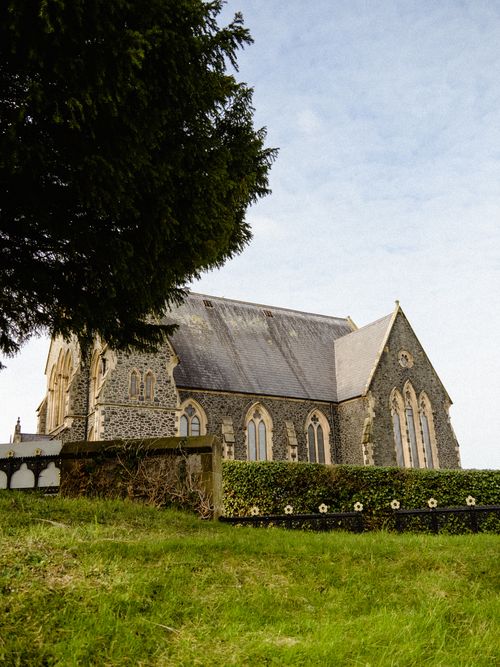 Free A serene view of an old stone church surrounded by greenery and clear skies. Stock Photo