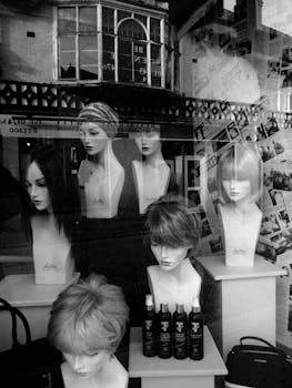 Vintage black and white storefront with mannequins displaying various hairstyles amidst hair products.